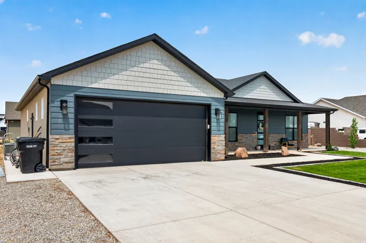 Modern exterior featuring a dark gray garage door with frosted panels, stone veneer accents, and a covered porch with dark wood columns
