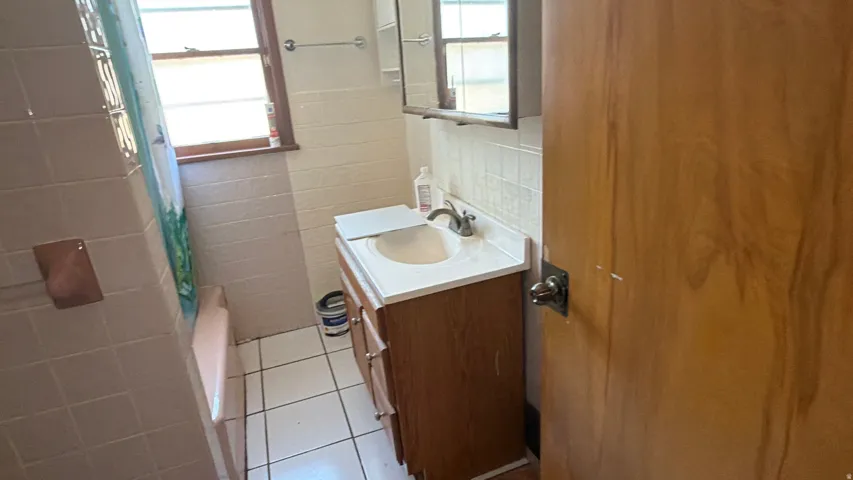 Bathroom featuring a single vanity with a laminate countertop, a mirrored medicine cabinet, and a tiled shower surround