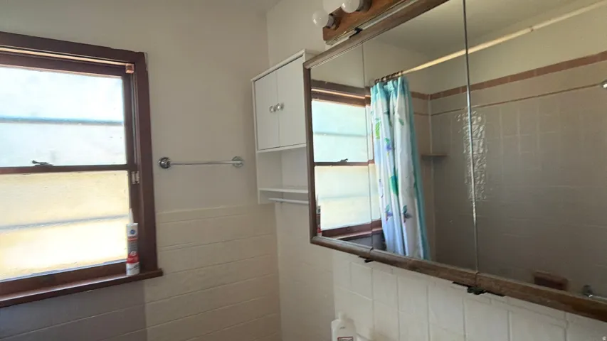Window with wood trim, wall-mounted towel bar, and a mirrored medicine cabinet with integrated lighting