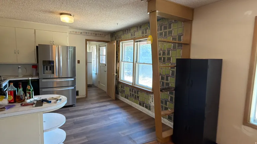 Stainless steel refrigerator, white cabinetry, integrated countertop seating, and wood-finish flooring