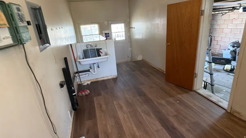 Wood-finish flooring with a utility sink, two windows, and an electrical service panel