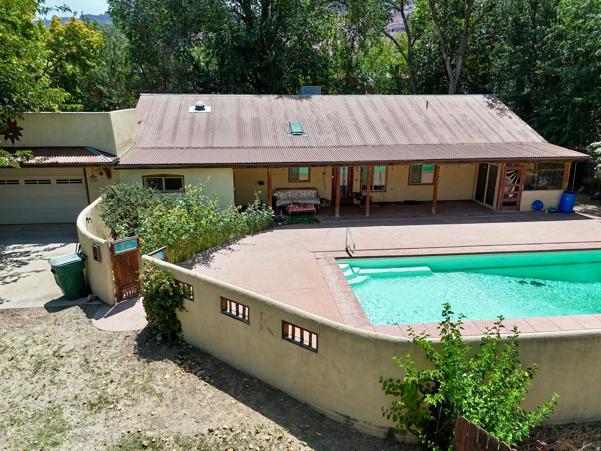 Corrugated metal roof, attached garage, curved stucco wall, expansive patio, and an in-ground swimming pool
