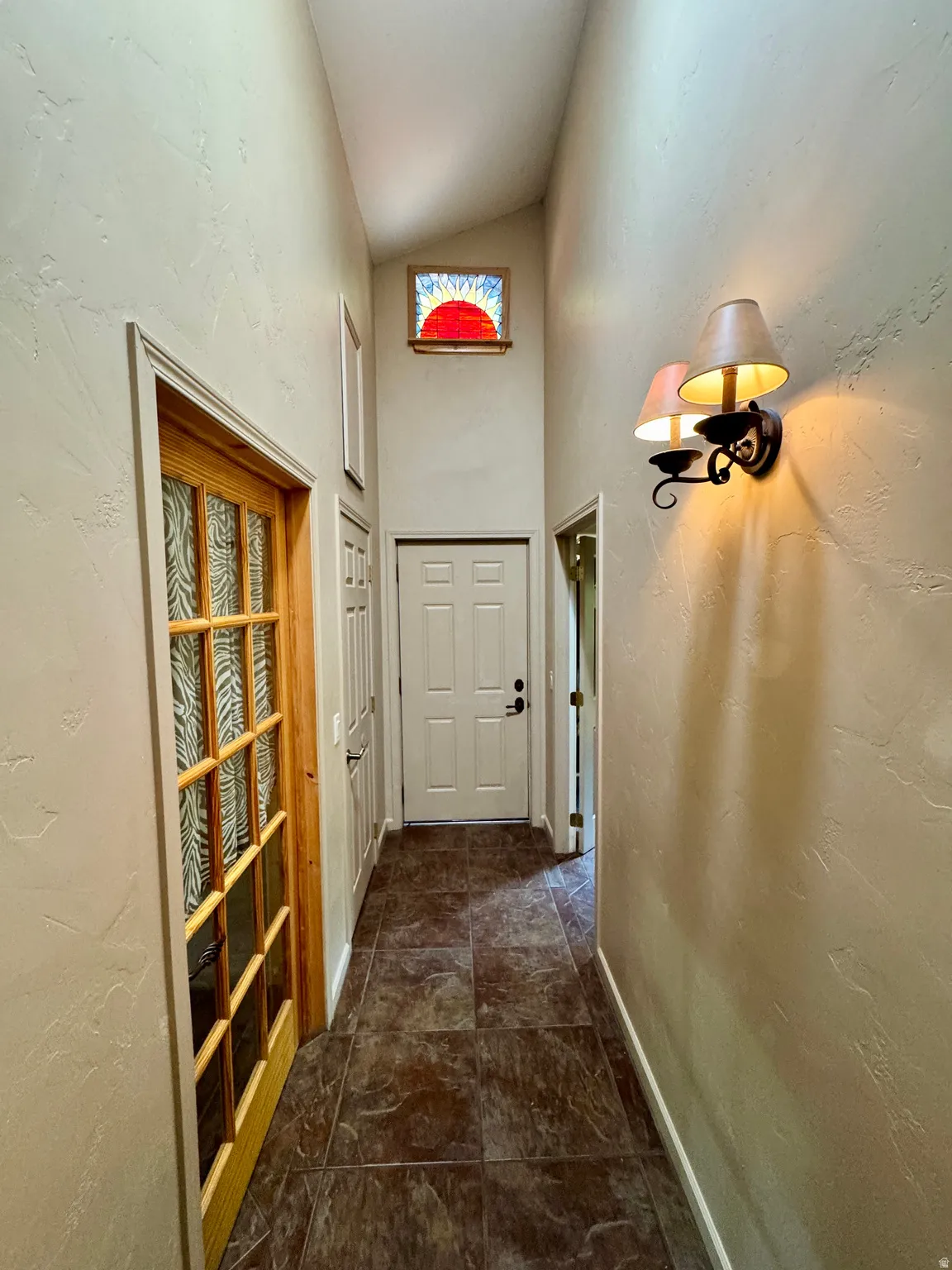 Textured wall finish, vaulted ceiling, decorative stained glass window, dark tile flooring, and wall-mounted sconce lighting