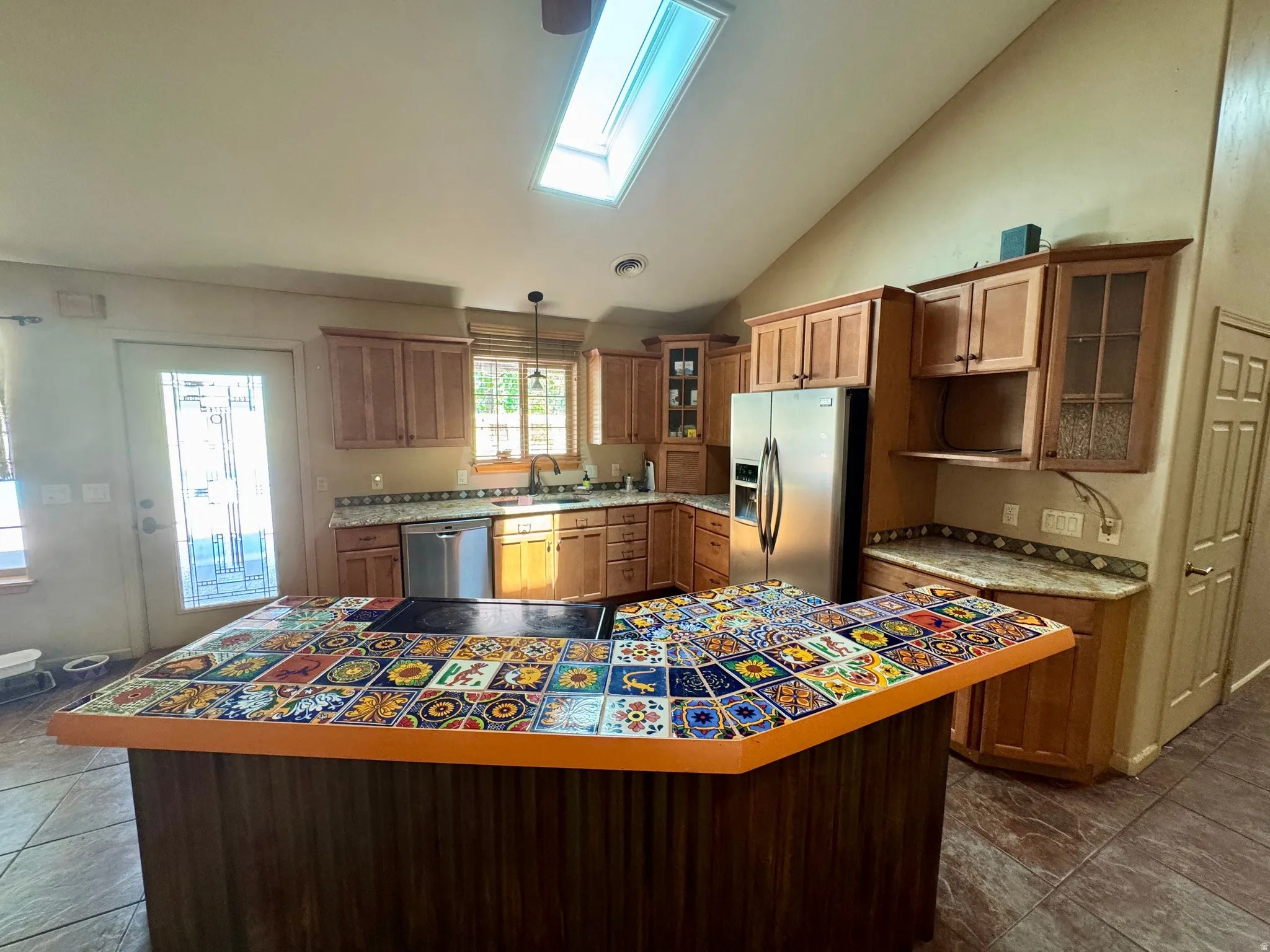 Spacious kitchen featuring custom wood cabinetry, stainless steel appliances, and a striking tile-topped island with warm wood-finish base