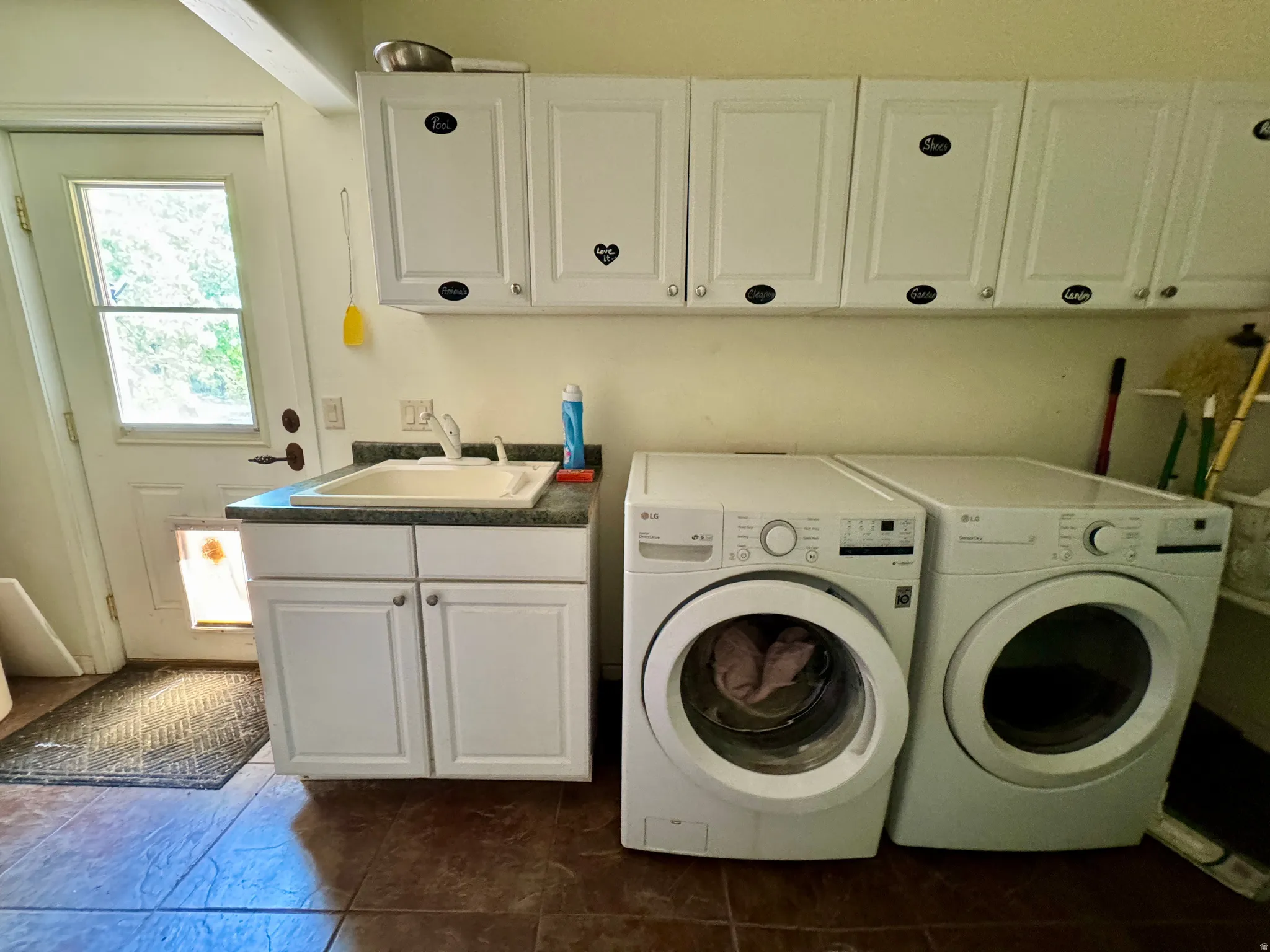 Utility room featuring a built-in sink, white cabinetry, and durable tile flooring