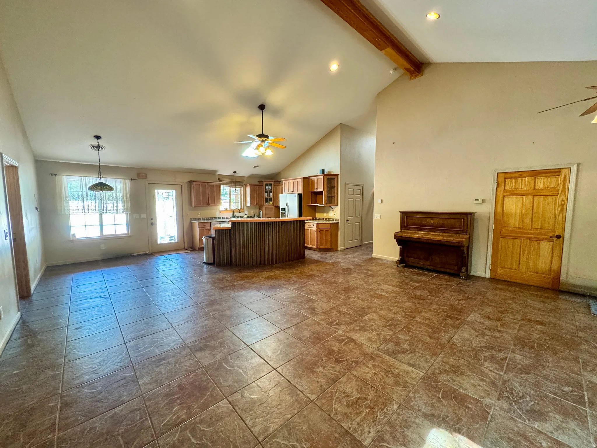 Spacious open-concept layout with tile flooring, vaulted ceilings, exposed wood beams, and a kitchen featuring wood cabinetry and a breakfast bar