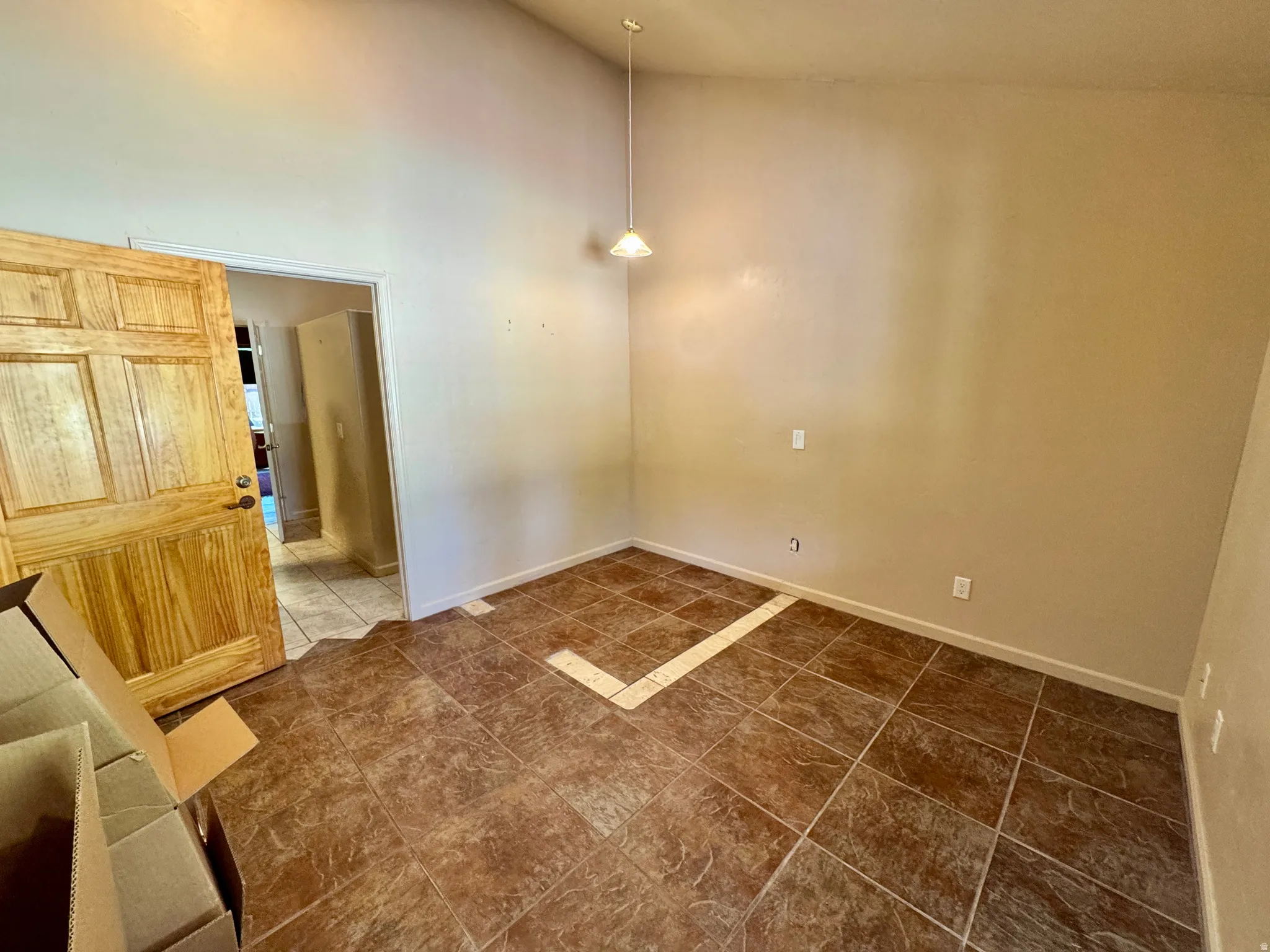 Vaulted ceiling with an attached light fixture, natural wood-finish door, and tile flooring