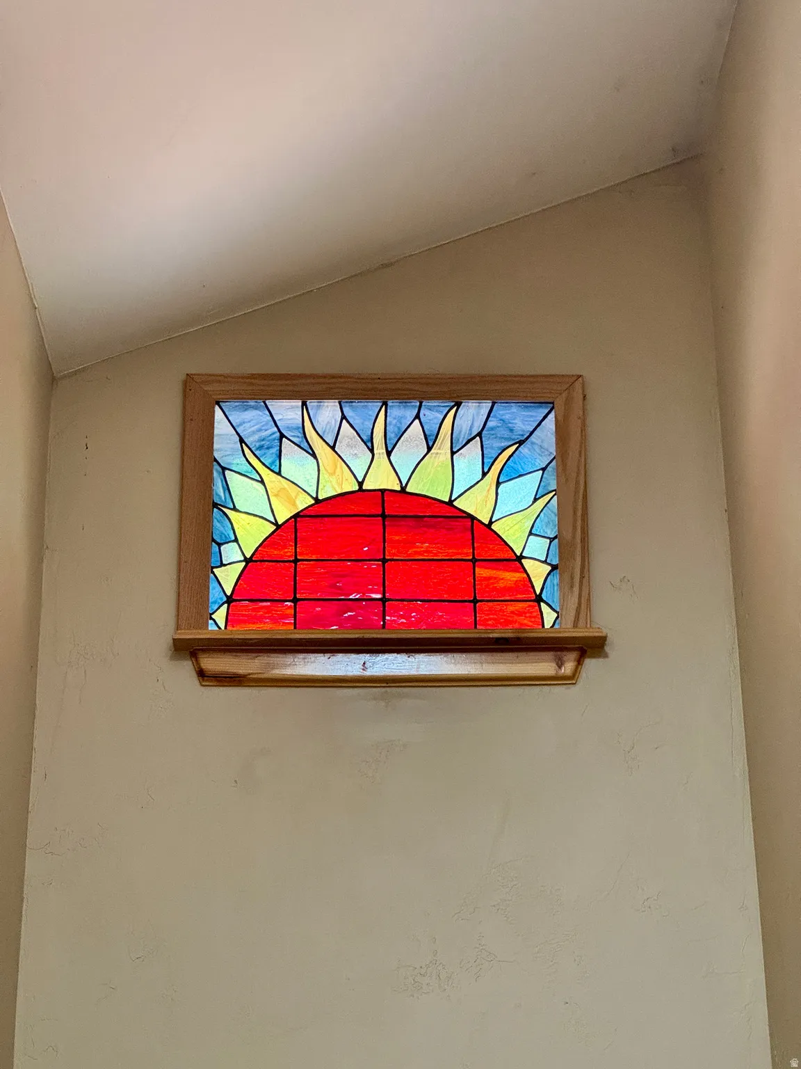 Stained glass window set in a wood frame, featuring a sun design with red, yellow, and blue hues