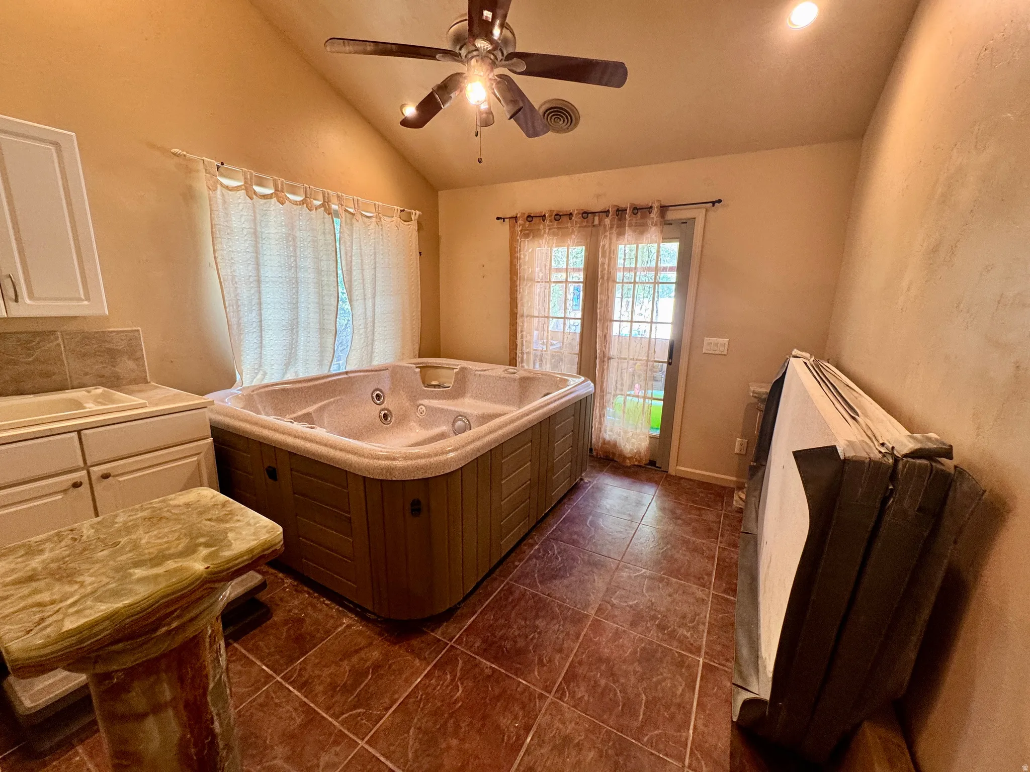 Spa tub with multiple jets, tiled flooring, vaulted ceiling, built-in cabinetry with sink, and French doors