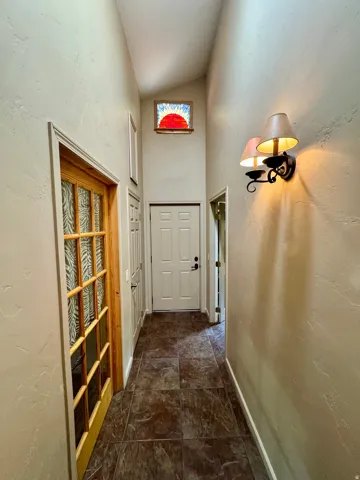 Textured wall finish, vaulted ceiling, decorative stained glass window, dark tile flooring, and wall-mounted sconce lighting