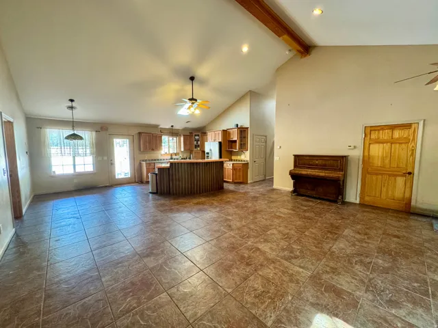 Spacious open-concept layout with tile flooring, vaulted ceilings, exposed wood beams, and a kitchen featuring wood cabinetry and a breakfast bar