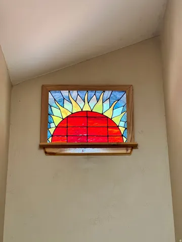 Stained glass window set in a wood frame, featuring a sun design with red, yellow, and blue hues