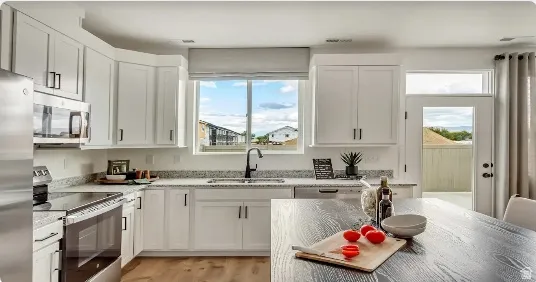 White cabinetry with matte black hardware, stainless steel appliances, granite countertops, and wood-finish flooring. This home is under construction. Pictures are of a similar home.