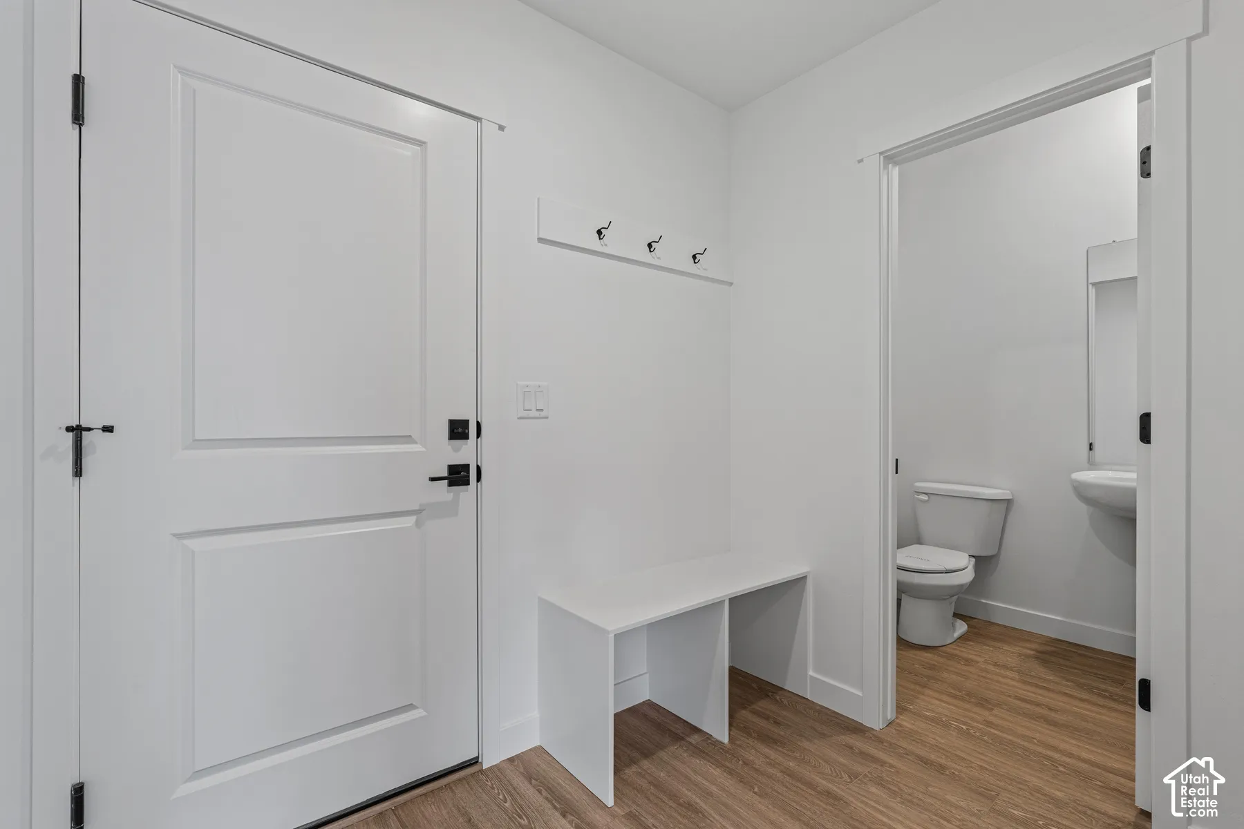 White paneled door with matte black hardware, wood-finish flooring, and white built-in bench