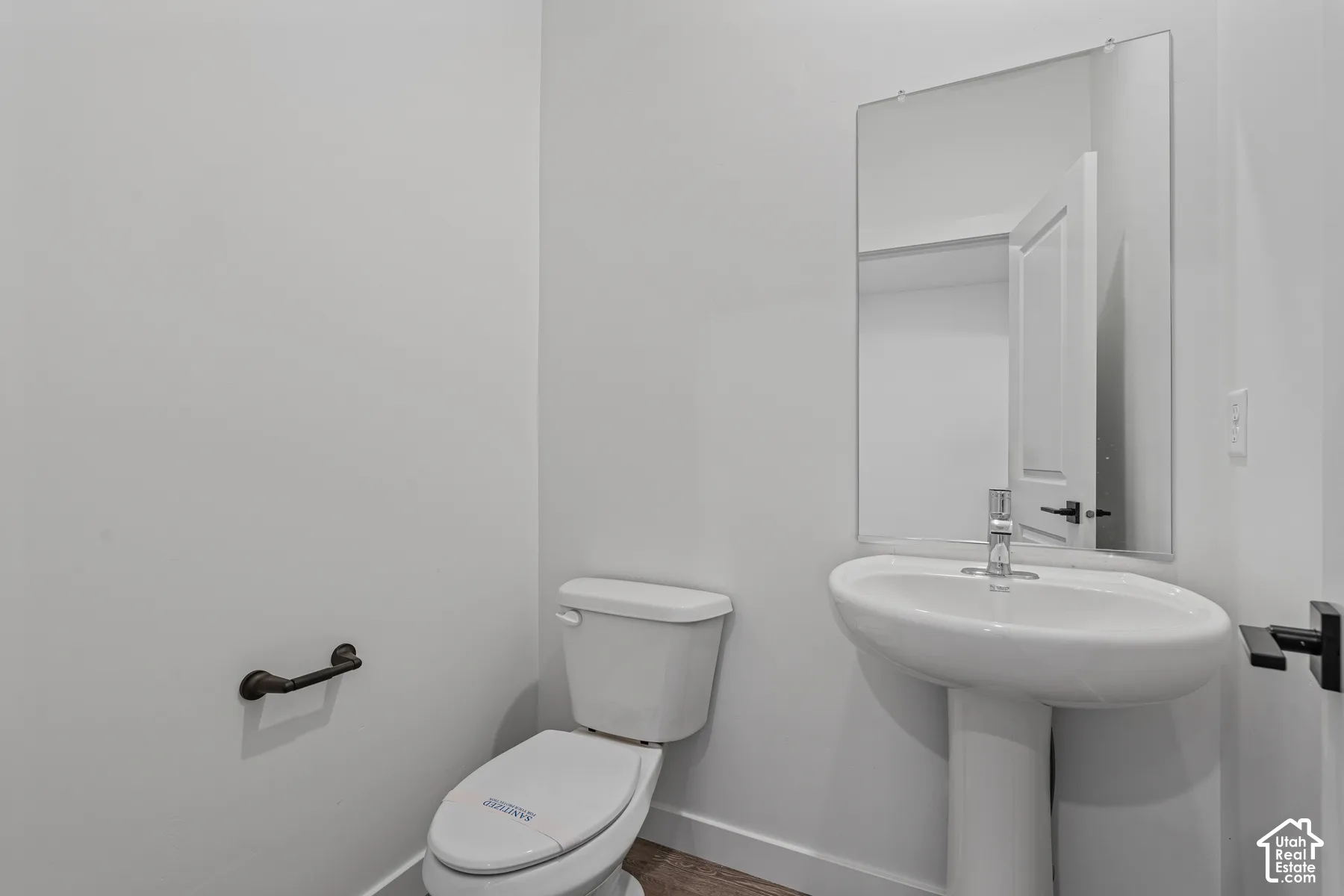 Pedestal sink with chrome faucet, wall-mounted mirror, and wood-finish flooring