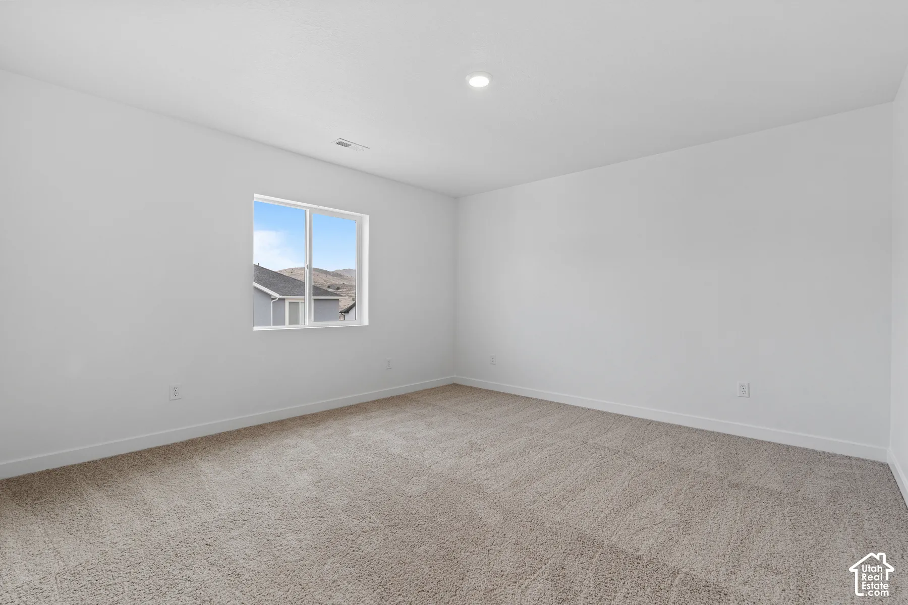 Recessed lighting, neutral-toned carpeting, white walls, and a large window
