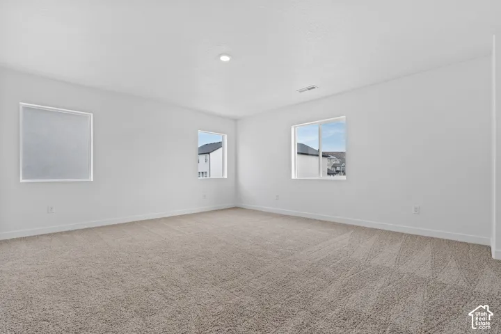 Neutral tone carpeting, white walls, recessed ceiling lighting, and multiple windows with white trim