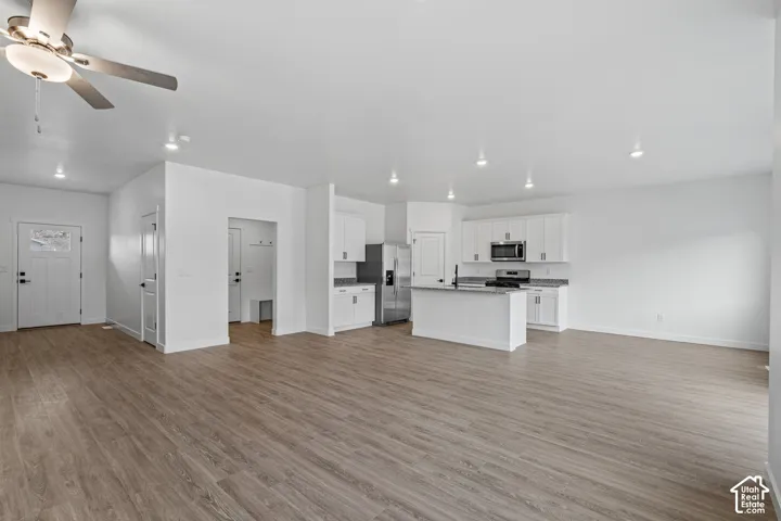 Open concept floorplan featuring wood-finish flooring, recessed lighting, a modern ceiling fan, and a kitchen with white cabinetry and stainless steel appliances