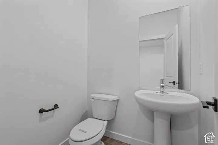 Pedestal sink with chrome faucet, wall-mounted mirror, and wood-finish flooring