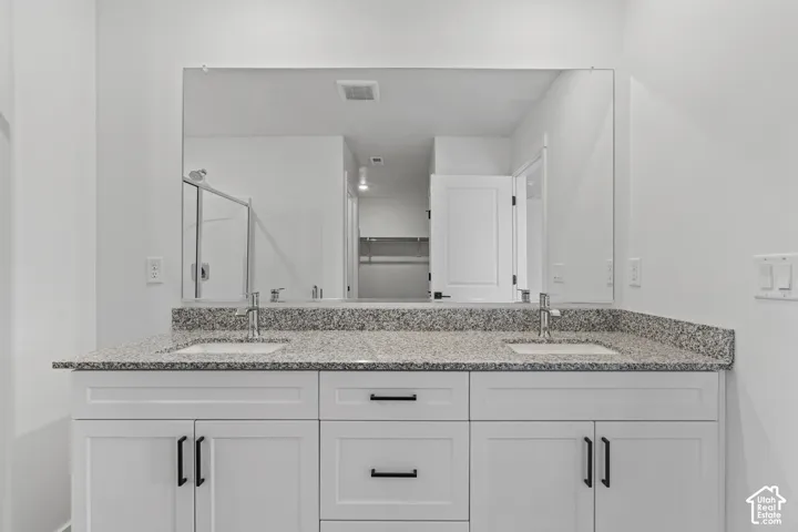 Dual vanity with undermount sinks, speckled countertop, white cabinetry with black hardware, and a large wall-mounted mirror