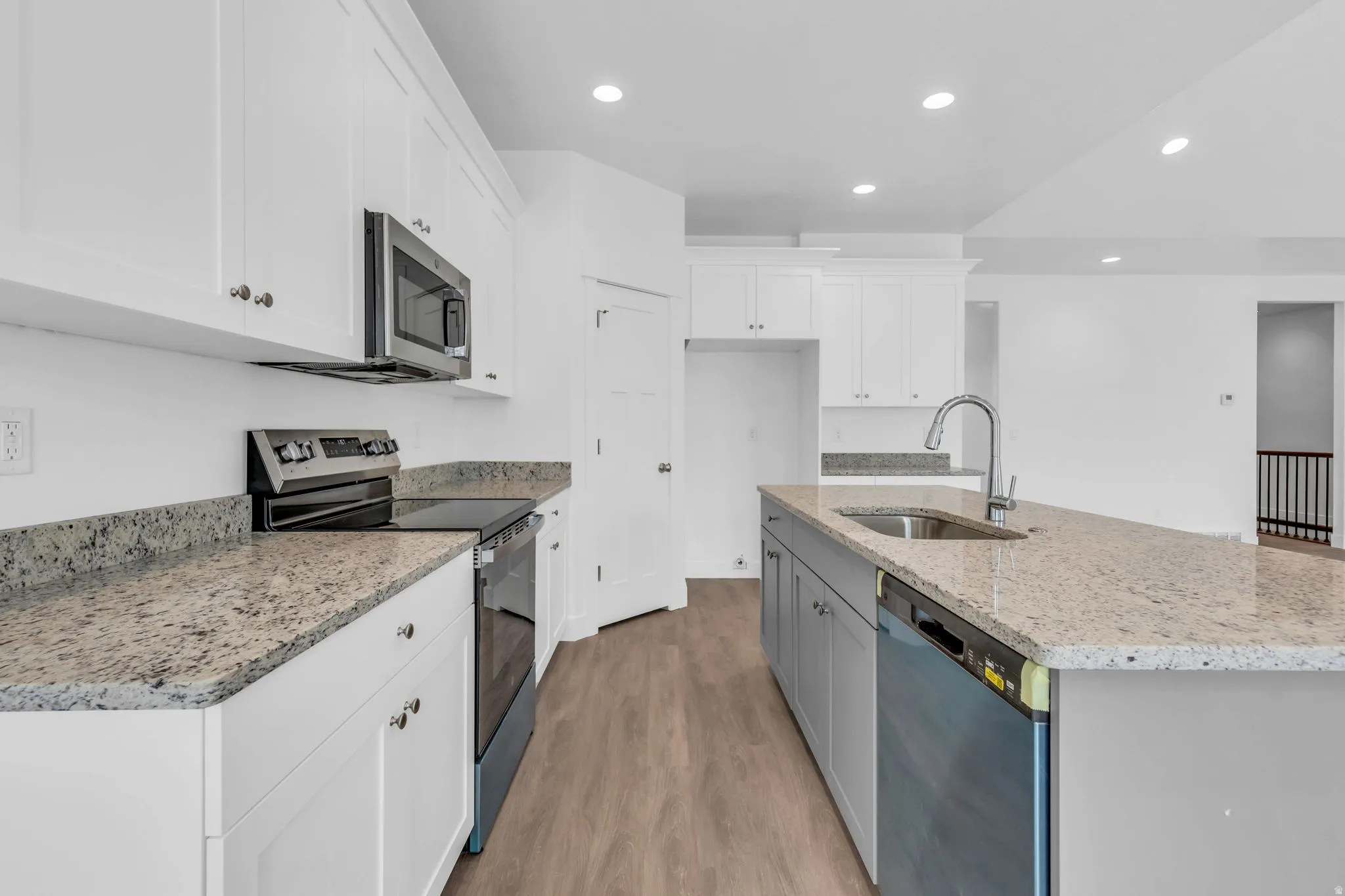 White shaker cabinetry, stone countertops, stainless steel appliances, wood-finish flooring, and recessed lighting