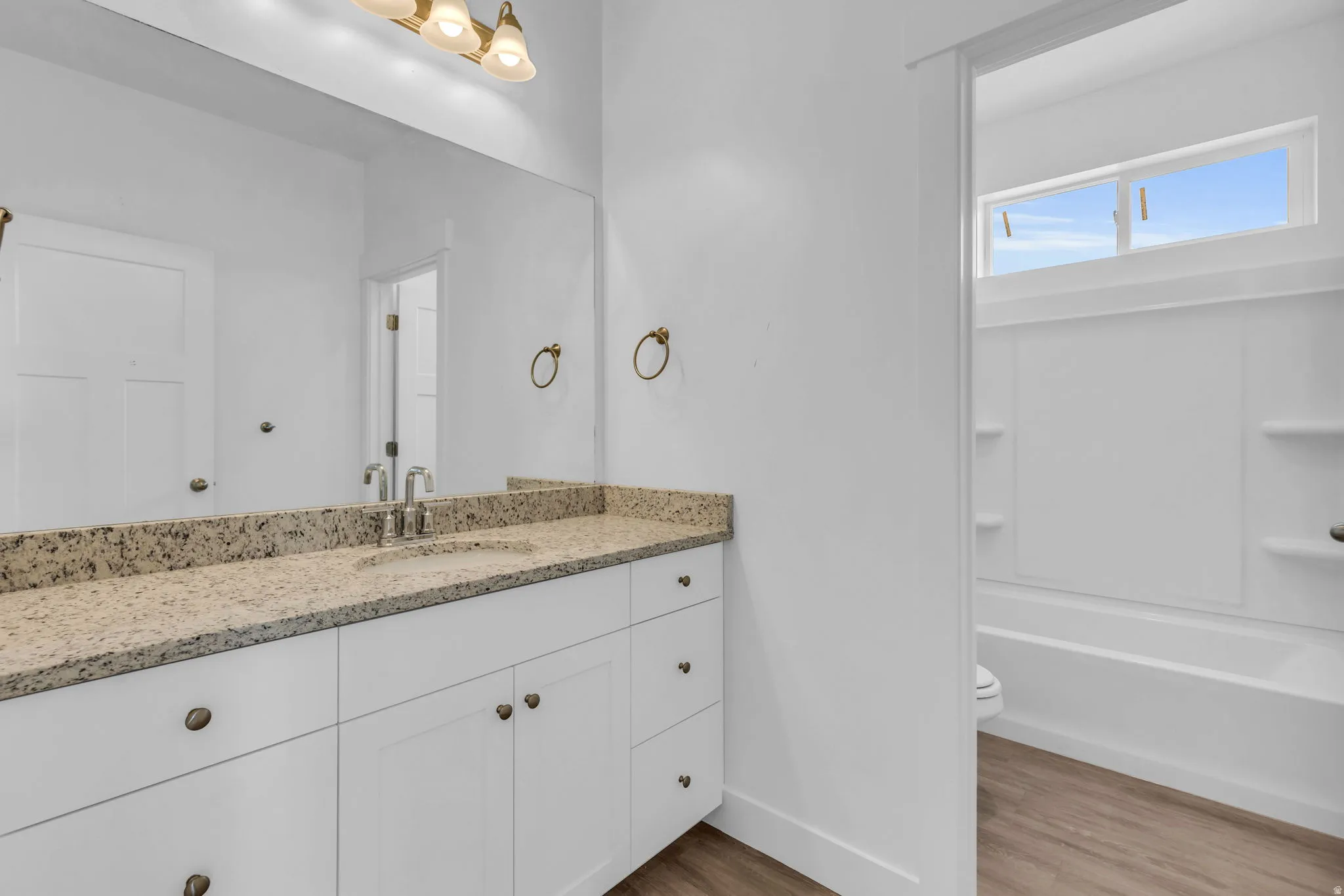 White vanity with brass hardware, light-toned countertop, and undermount sink