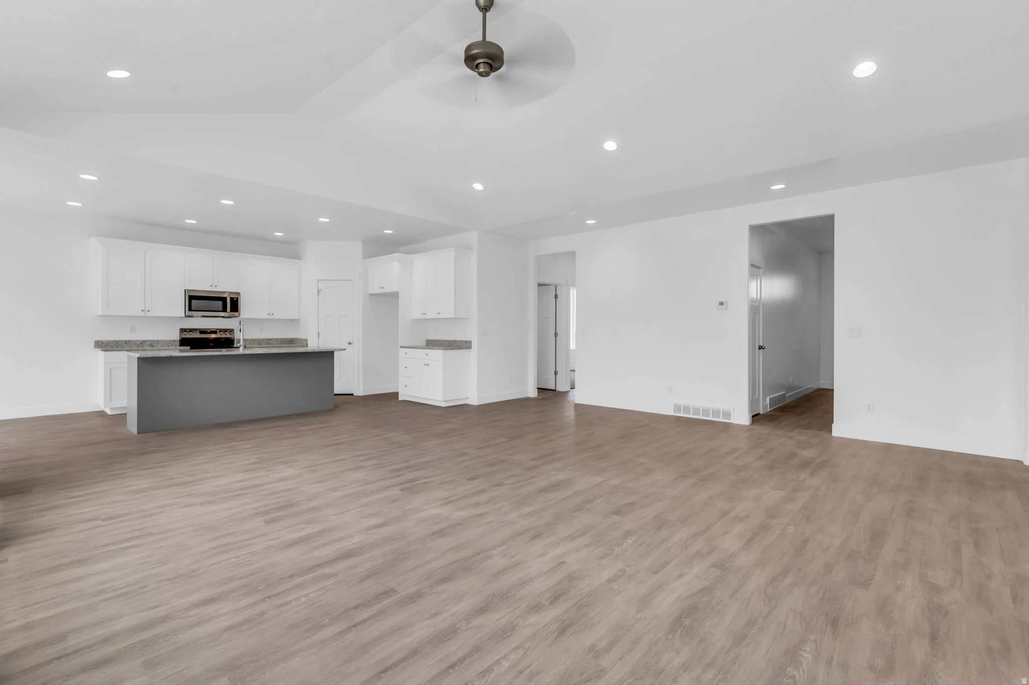 Spacious open-concept living area with wood-finish flooring, recessed lighting, and a ceiling fan