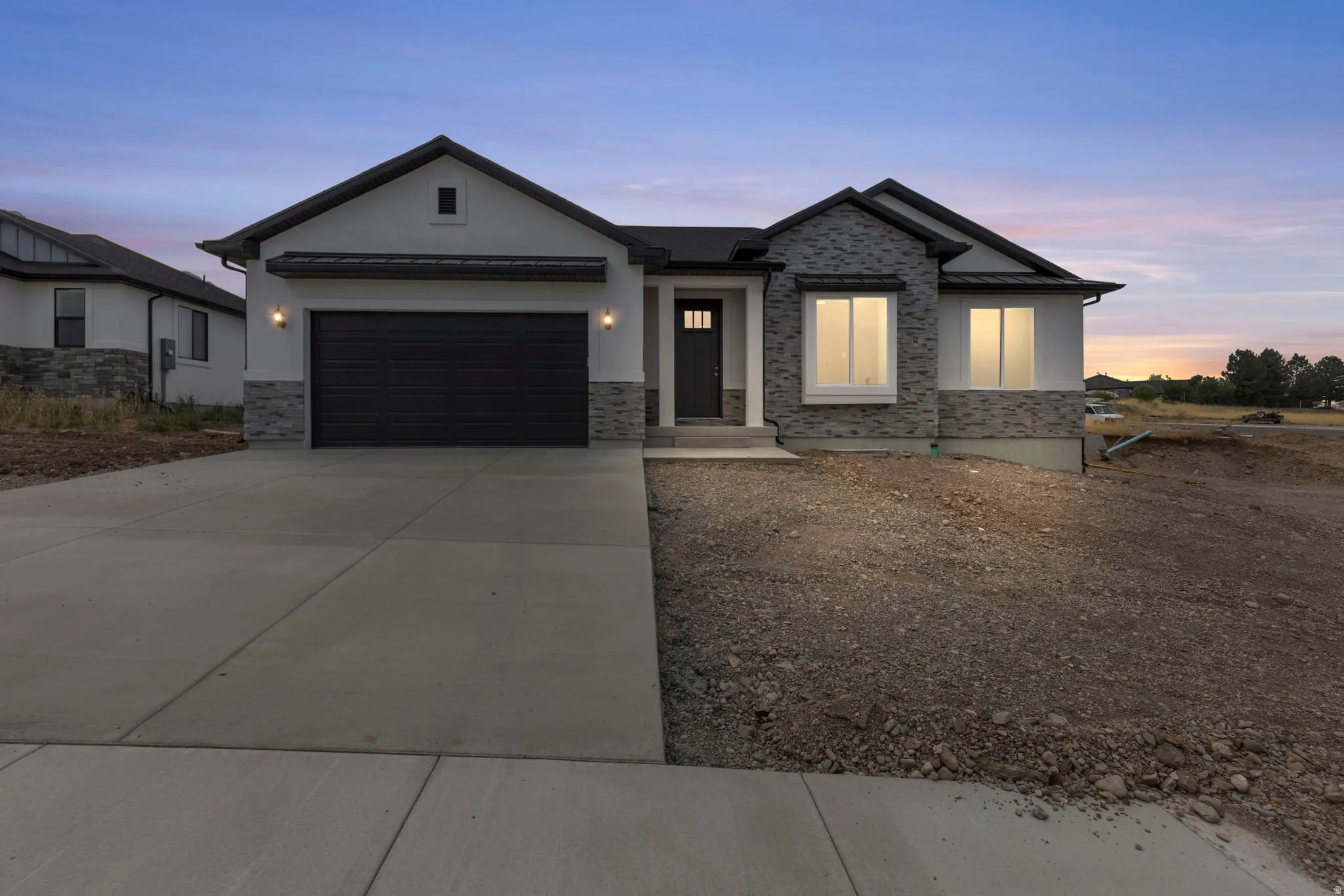 Stucco and stone facade with a dark gray garage door, a covered entry, and a concrete driveway