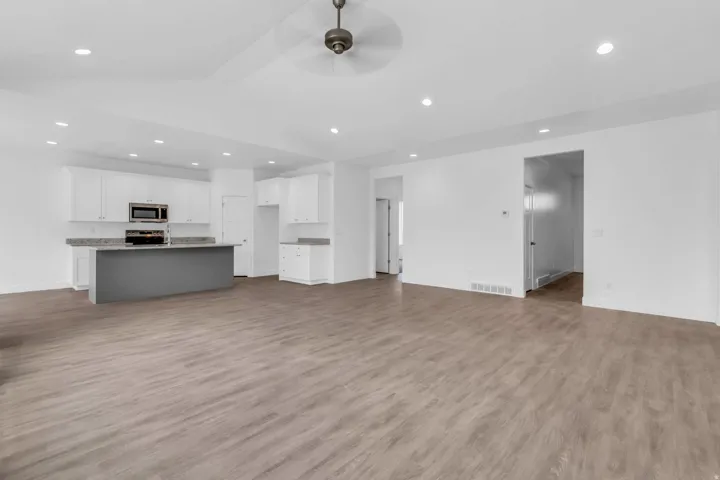 Spacious open-concept living area with wood-finish flooring, recessed lighting, and a ceiling fan