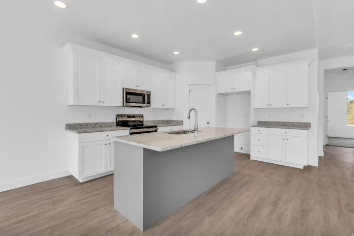 Kitchen featuring white shaker cabinetry, stainless steel appliances, light-toned countertops, a central island with a sink, and wood-finish flooring