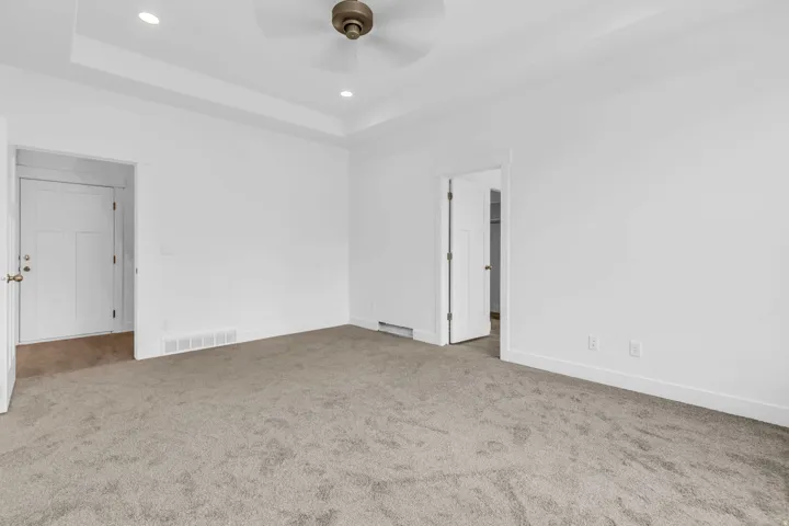 Spacious room featuring neutral carpeting, white painted walls, a tray ceiling with recessed lighting, and a ceiling fan