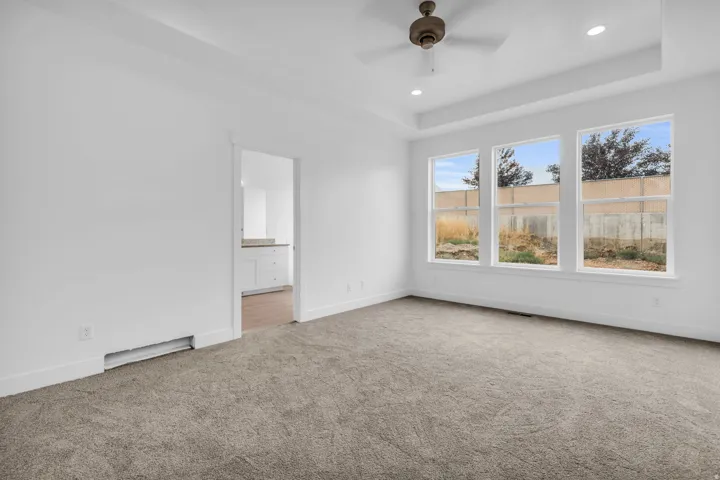 Tray ceiling with recessed lighting, ceiling fan, three large windows, gray carpet, and white baseboards