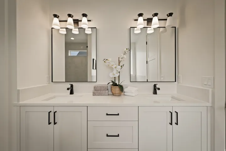 Primary bathroom features a dual vanity with white shaker-style cabinetry, matte black hardware, and integrated sinks