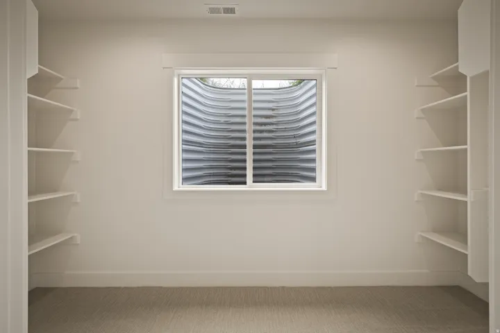 Built-in shelving, egress window, neutral wall paint, white trim, and carpeted flooring
