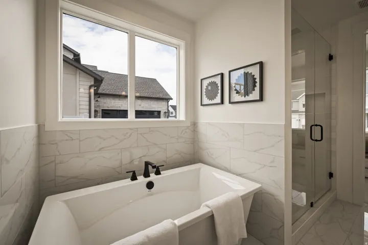 Primary bath includes a freestanding tub with matte black fixtures, white marble-look wall tiling, and a glass-enclosed shower