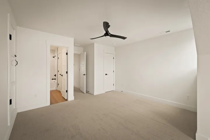 Neutral-toned carpeting with white walls, black ceiling fan, and white doors with black hardware