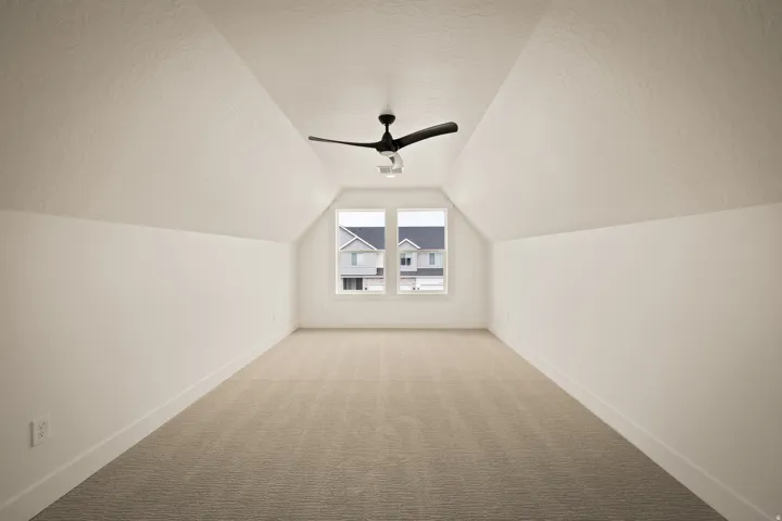 Attic space featuring sloped ceilings, a central ceiling fan, twin windows, and carpeted flooring