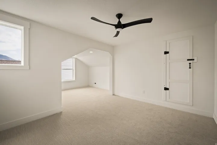 Carpeted flooring, vaulted ceiling, black ceiling fan, white trim, and a built-in wall door with black hardware