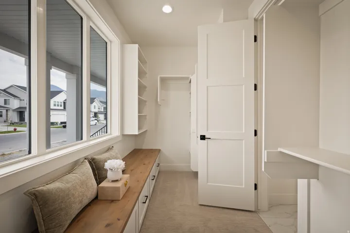 Built-in window bench with wood-finish top and integrated storage, multiple windows providing natural illumination, white built-in shelving, white paneled door with matte black hardware, and an additional built-in shelf