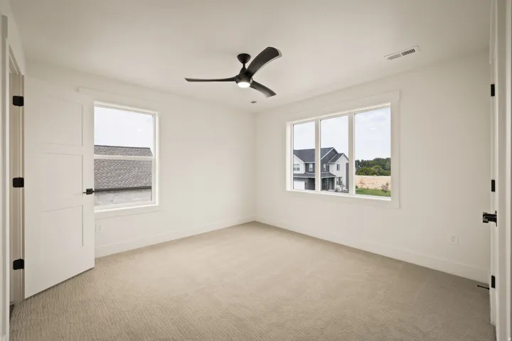 Bright secondary bedroom upstairs offers dual windows with natural light, neutral carpet flooring, and a ceiling fan