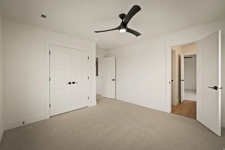 Light-toned carpeted flooring complements white walls, featuring white paneled doors with matte black hardware and a ceiling fan with integrated lighting