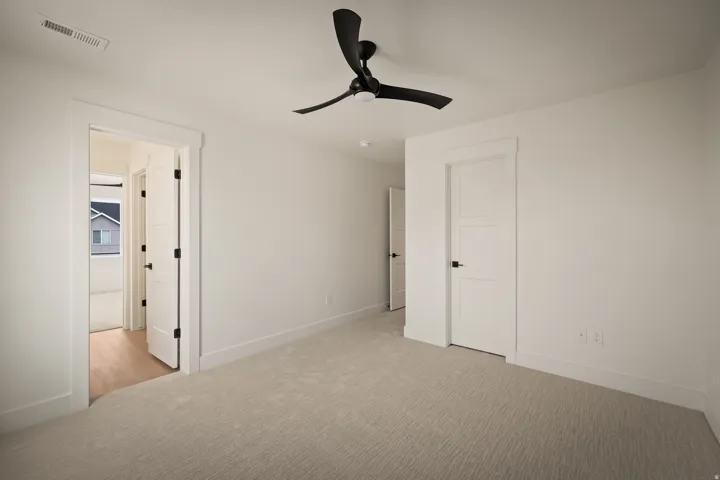 Light-toned wall-to-wall carpeting, white walls, white trim, and a black ceiling fan