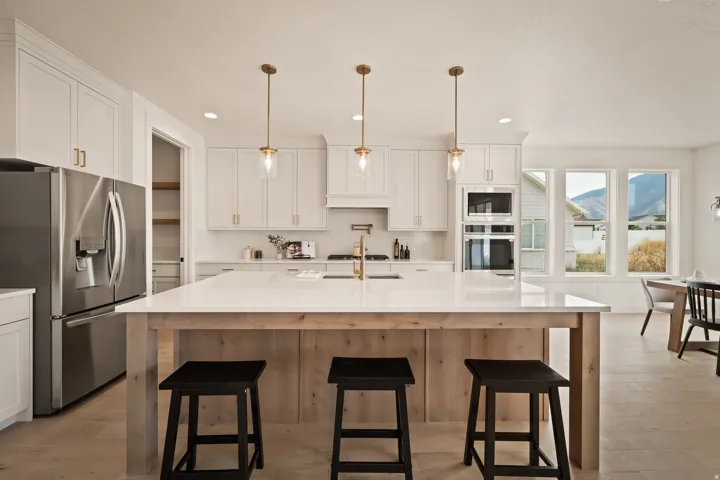 White shaker cabinetry, built-in stainless steel appliances, large kitchen island with seating, pendant lighting, and light wood-finish flooring