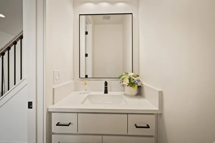 Main floor half bathroom, white vanity with integrated sink, matte black faucet, and a large framed mirror