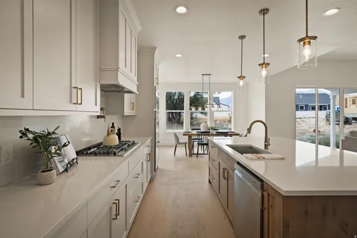 Gourmet kitchen featuring a gas range, white cabinetry, a large center island with an undermount sink, pendant lighting, and light wood-finish flooring