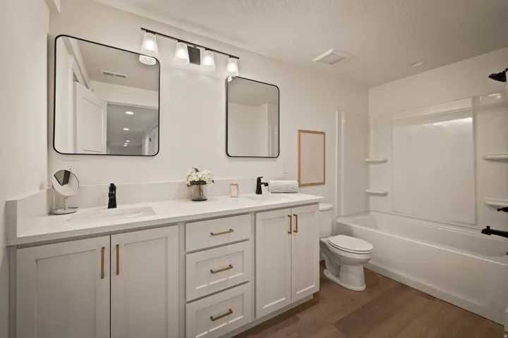 Dual vanity with white shaker-style cabinetry, matte black fixtures, and wood-finish flooring