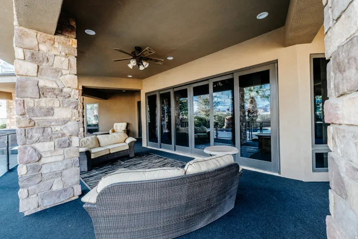 Expansive covered patio featuring stone columns, a ceiling fan, and multiple glass folding doors