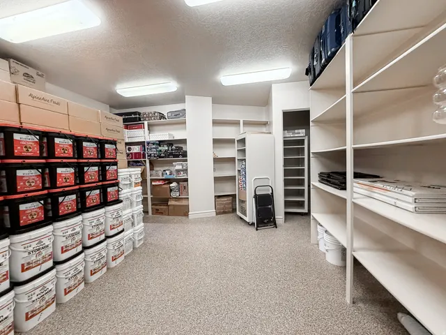 Spacious storage room featuring extensive built-in shelving, durable speckled flooring, and integrated ceiling lighting