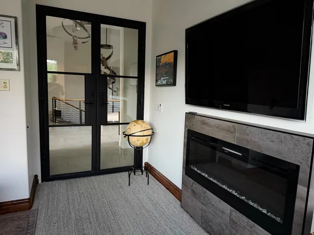Black-framed glass French doors, modern fireplace with a tiled surround, light-colored flooring, and dark wood-finish trim