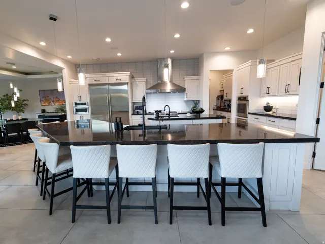 Expansive kitchen island featuring a dark countertop, white shaker cabinetry, stainless steel appliances, and integrated lighting